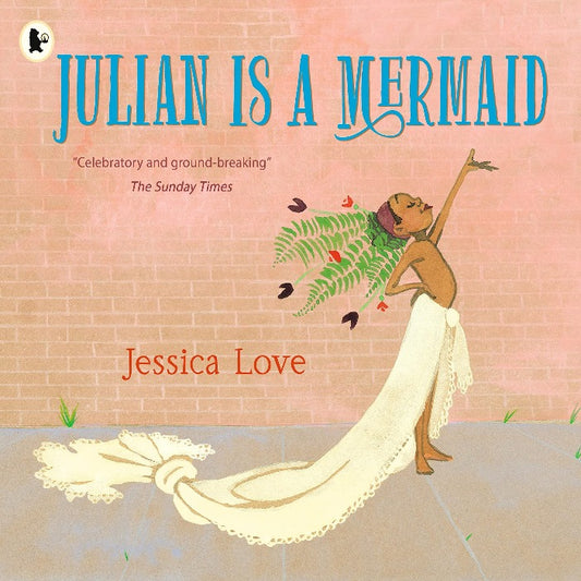 Julian, a young boy with short curly hair and a big smile, stands in his living room surrounded by flowing blue curtains and colorful fish decorations. He wears a green tank top and a flower necklace, holding a fern in one hand and a seashell in the other. In the background, two women with afros look on lovingly. A magical and uplifting story about self-expression and acceptance